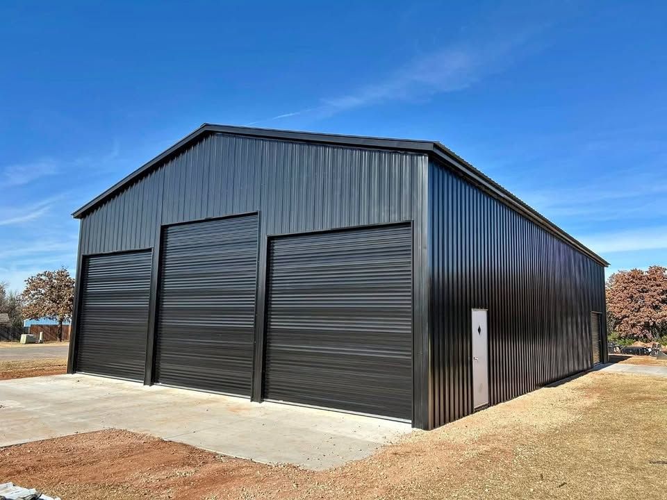 Black metal building with three garage doors against a blue sky.