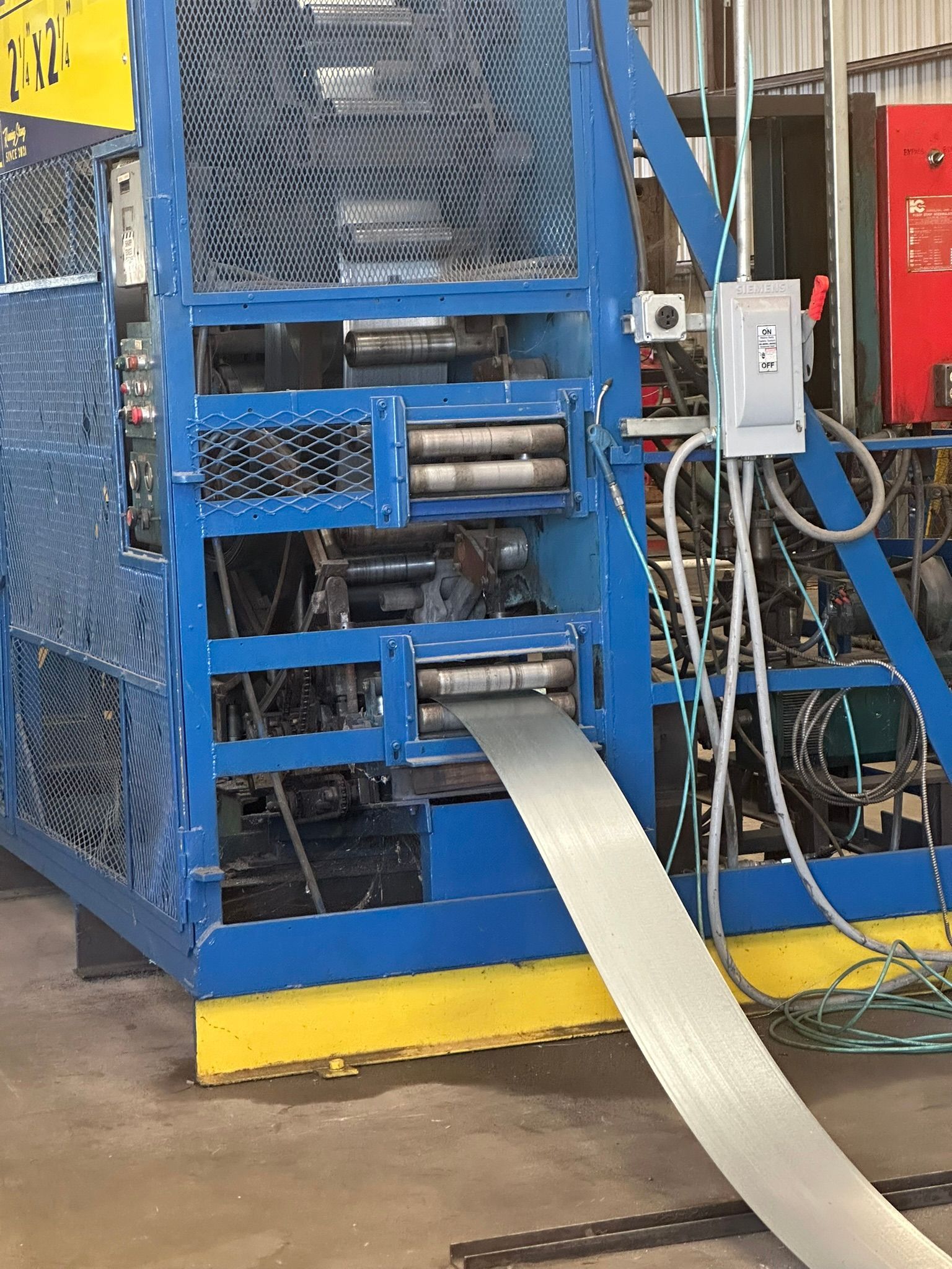 Blue industrial machine shaping metal strip in a factory setting.