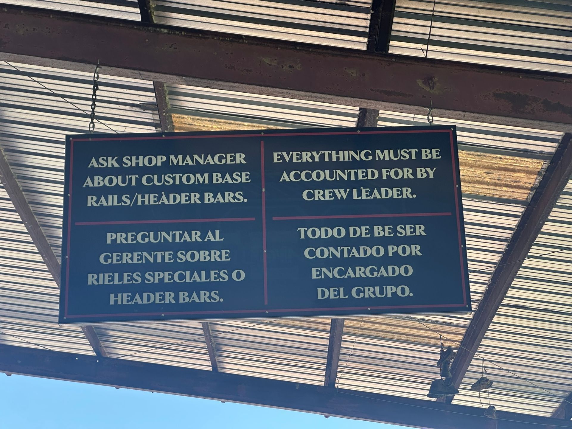Sign with English and Spanish text, under a corrugated metal roof.