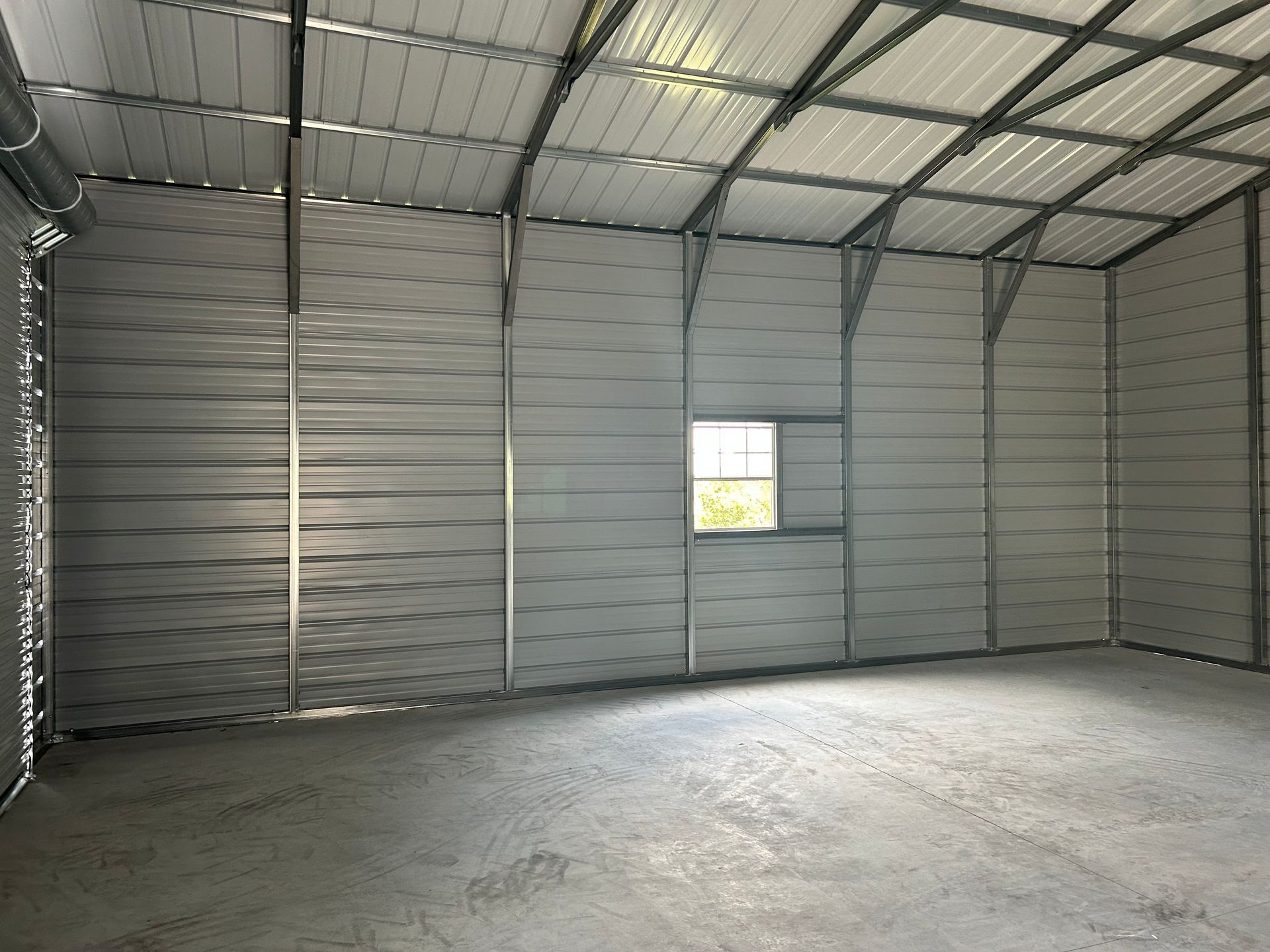 Interior of a metal building with gray walls, concrete floor, window, and exposed steel frame.