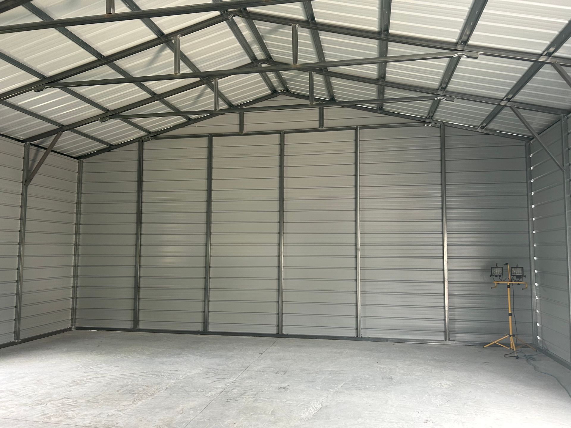 Interior view of a large, empty metal shed with a gravel floor and a visible structural frame.