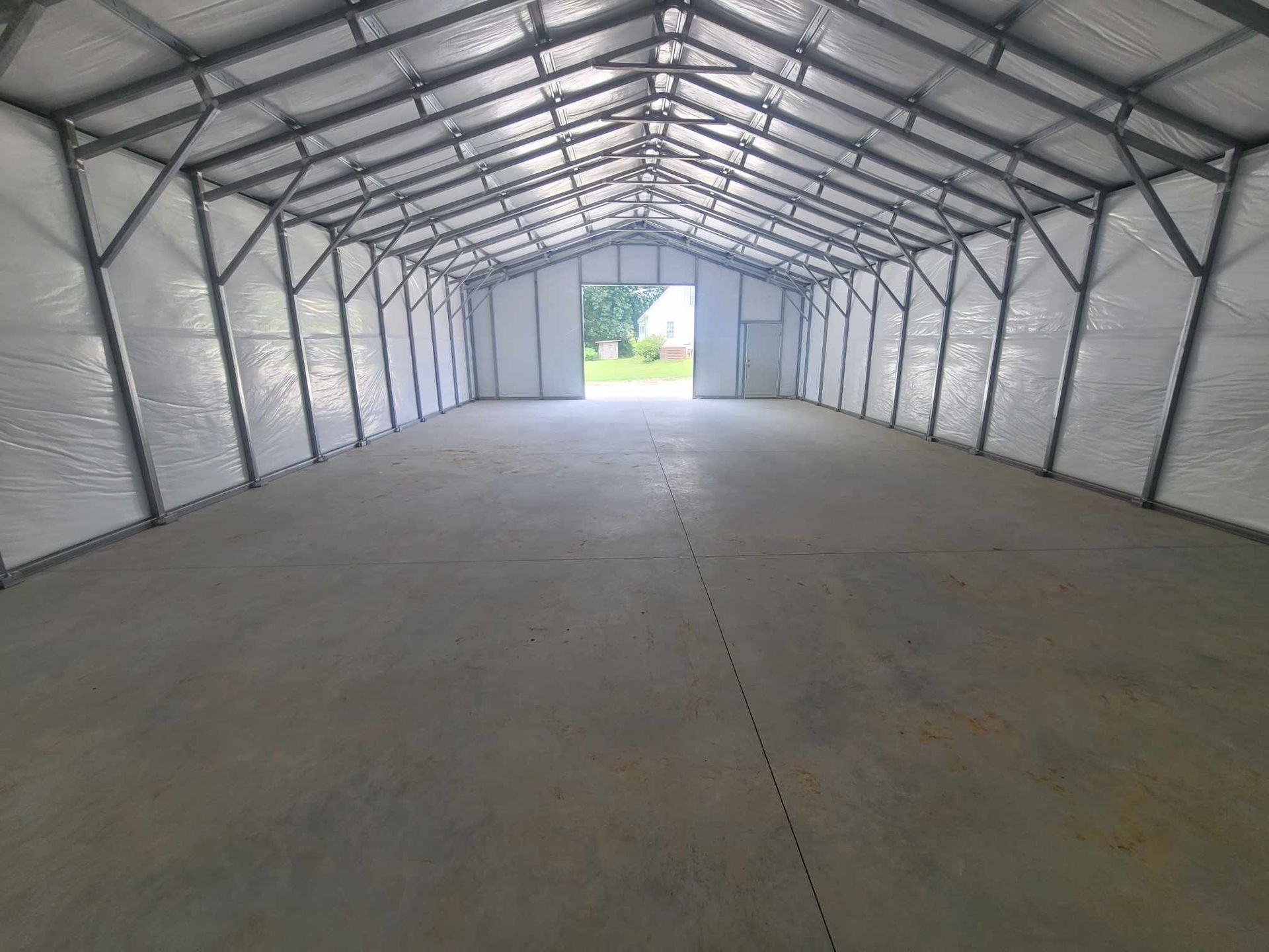 Inside of a large, empty metal building with concrete floor; door at far end open to bright light.