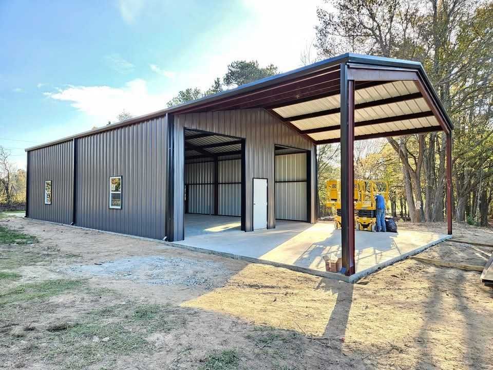 Metal workshop building with an attached awning; gray walls, maroon trim, on a concrete slab.