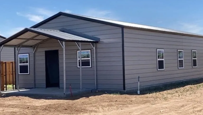 Gray metal building with a covered porch, windows, and a blue sky backdrop.