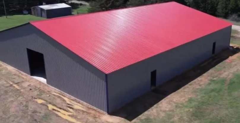 A large metal building with gray walls and a bright red roof, in a grassy outdoor setting.