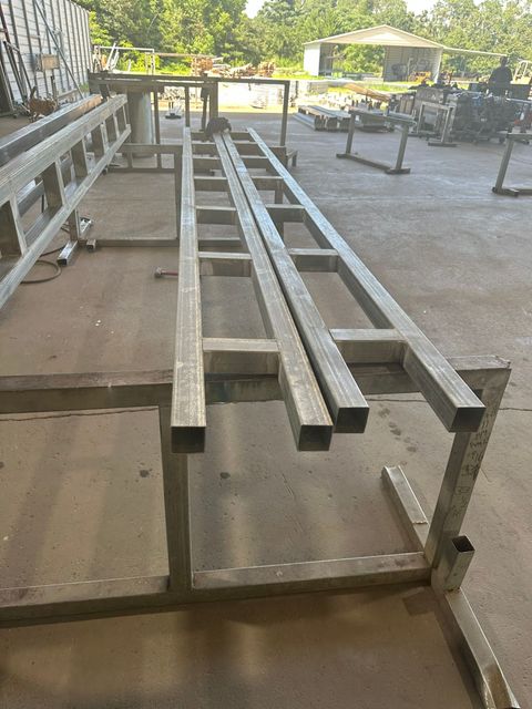 Metal beams stacked on a metal rack in an industrial outdoor setting.