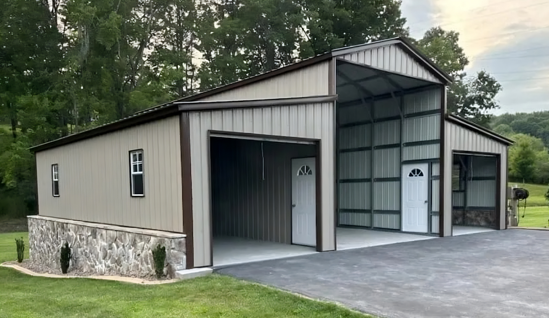 Tan and brown metal barn with two open bays, white doors, and stone accents. Set on asphalt and grass.
