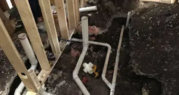 Plumbing pipes in trench with wooden framing; construction site.