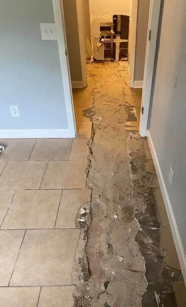 Hallway with damaged tile, debris scattered. A doorway leads to a kitchen area with appliances.