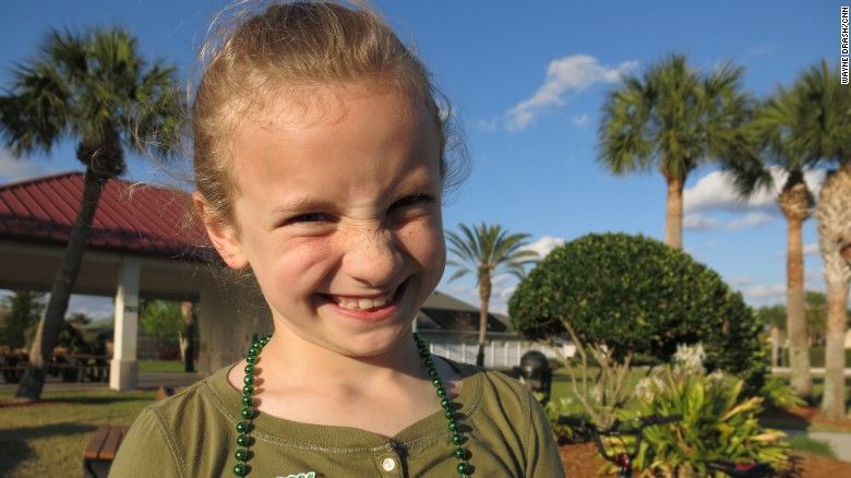 A little girl wearing a green necklace is making a funny face.