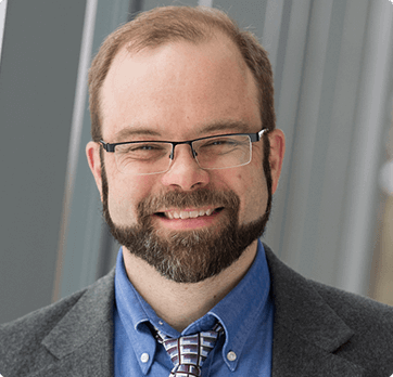 A man with a beard and glasses is smiling for the camera