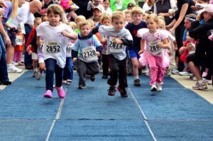 A group of children are running in a race with numbers on their shirts