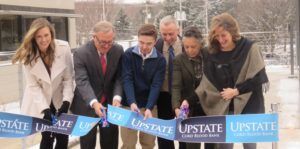 A group of people are cutting a ribbon that says upstate on it.