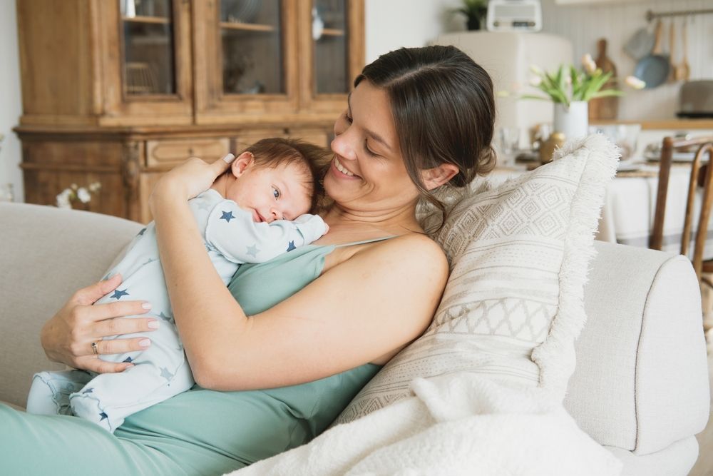 A woman is sitting on a couch holding a baby.