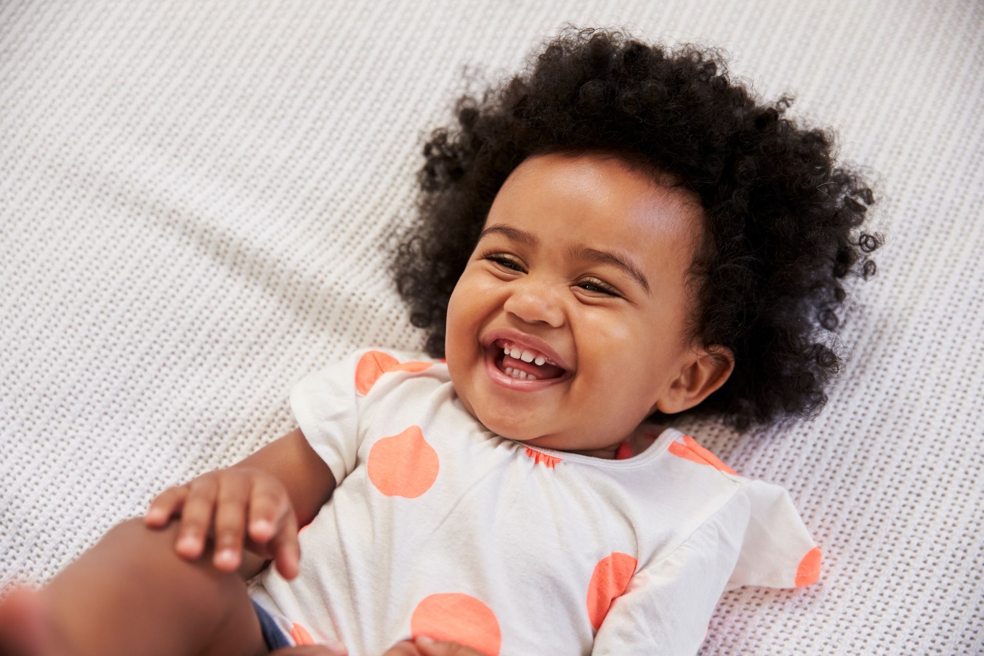 A baby is laying on a bed and smiling.