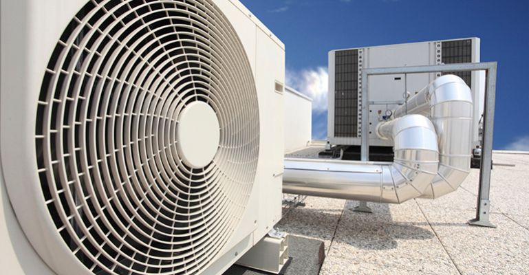 HVAC technician in red shirt and cap installing an air conditioning unit on a white house exterior.