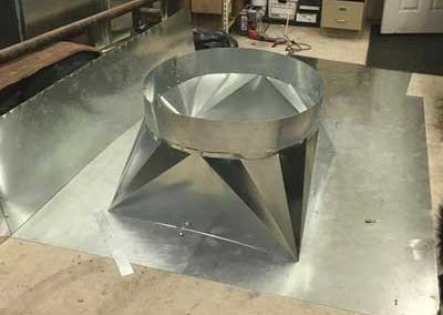 Metal ductwork component on a metal sheet in a workshop.