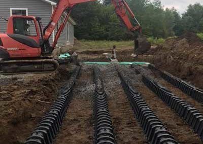 Red excavator installing a septic system with black drainfield pipes in a residential yard.