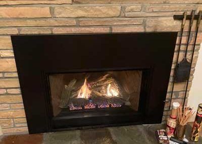 A fireplace with a black surround, burning fire, set into a stone wall.