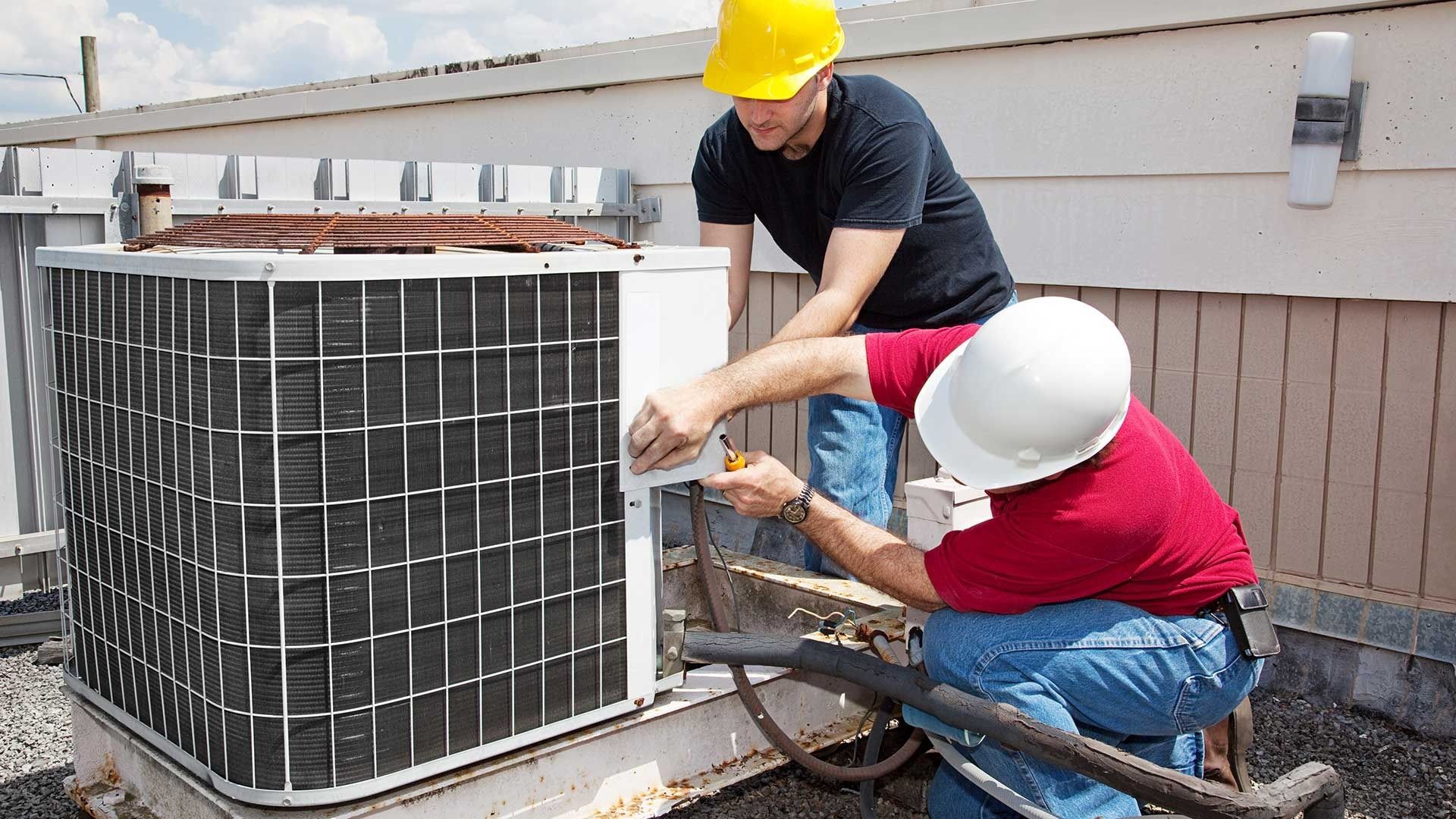 Two HVAC technicians working on an air conditioning unit on a rooftop.