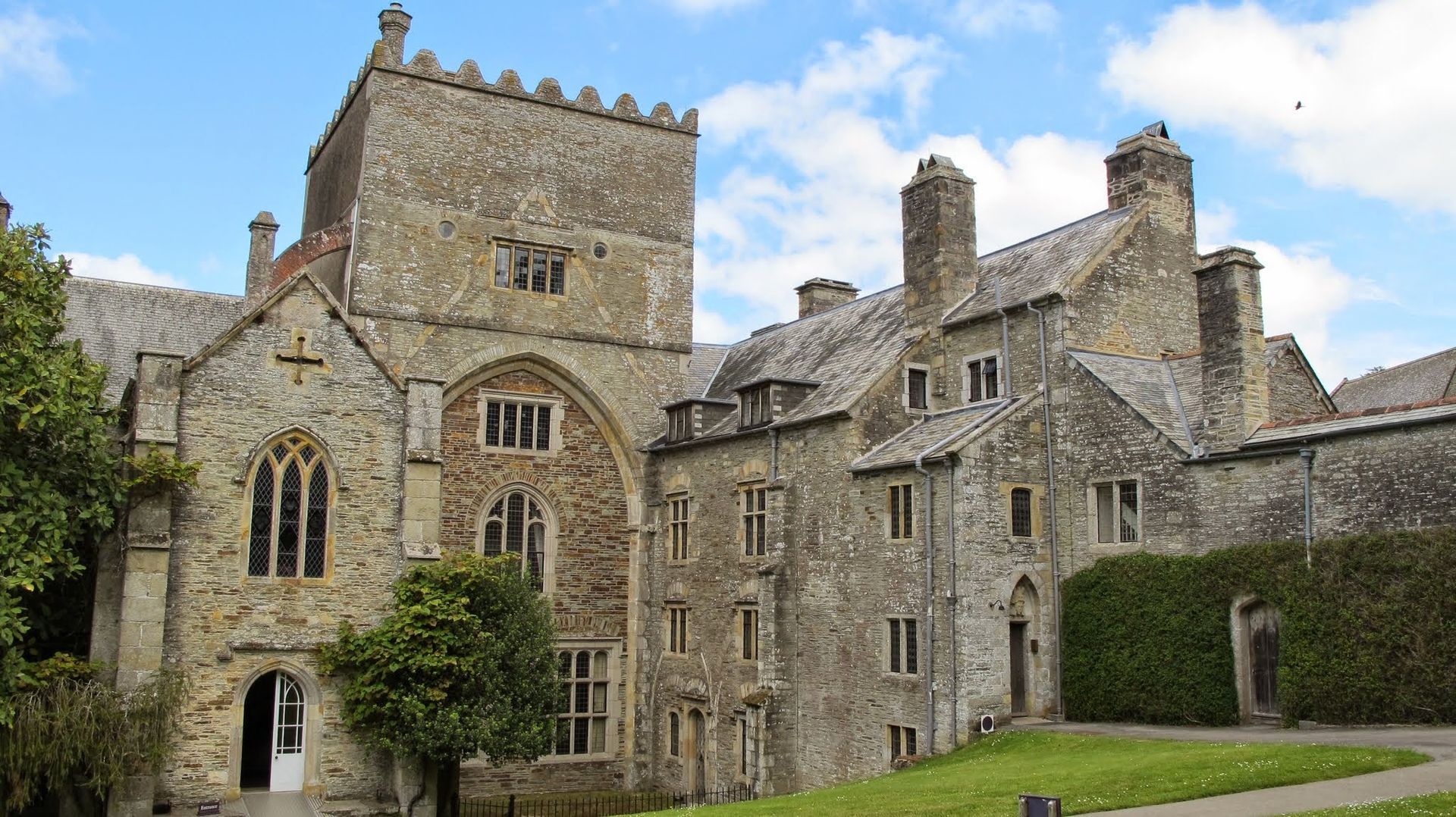 Stone abbey building with a large tower, arched doorway, and windows under a partly cloudy sky.