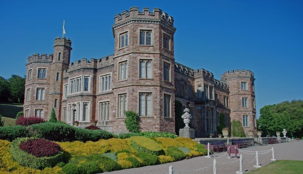 Castle with turrets and manicured gardens against a blue sky.