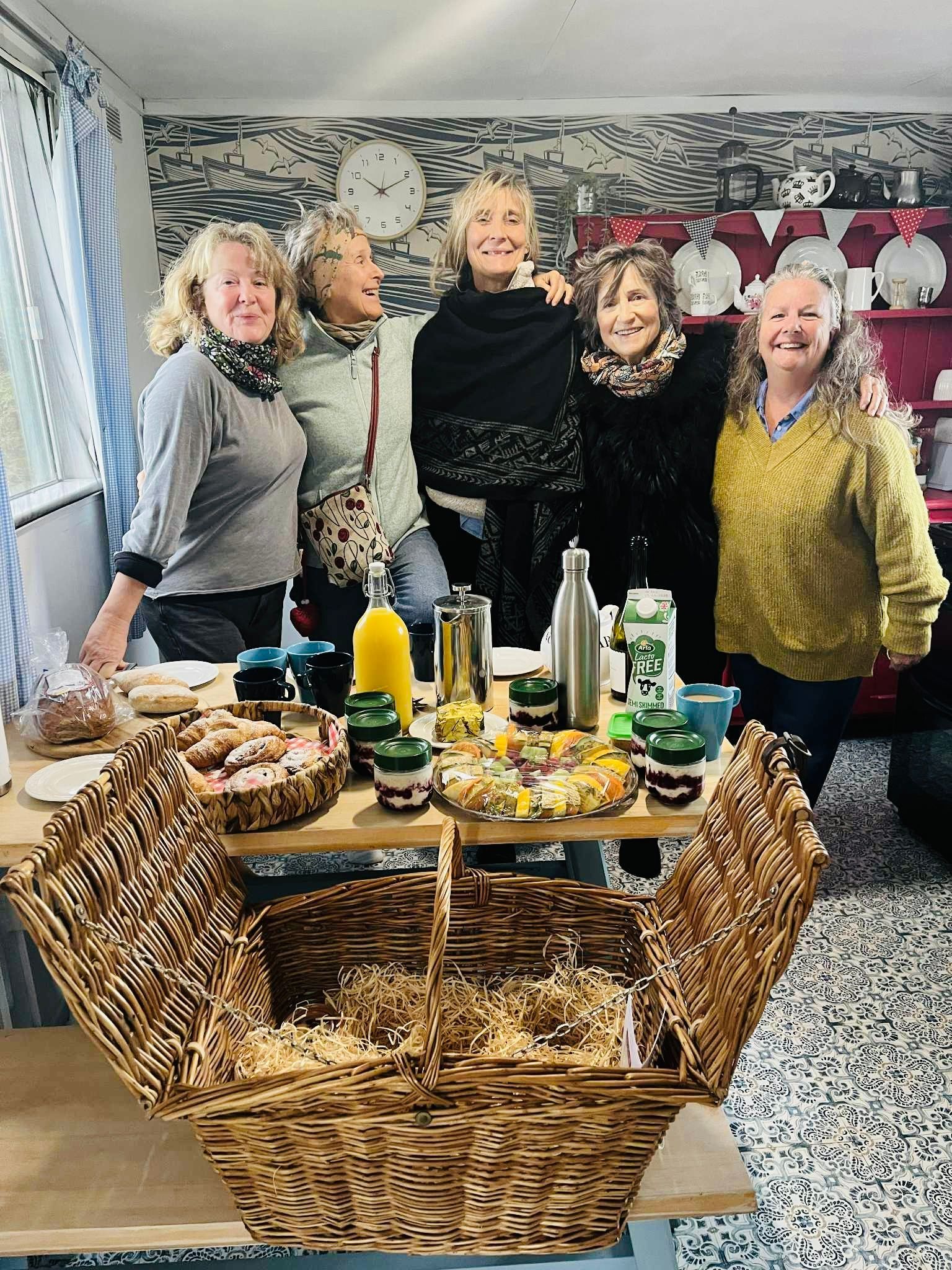 Group gathered around the table in the shared farmhouse kitchen with breakfast hamper at Coastal Glamping Cornwall
