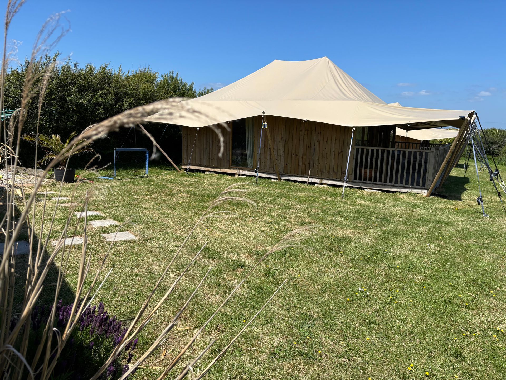 Cozy outdoor room with wicker furniture, a rug, and a macrame chandelier. Wooden walls, corrugated metal roof.