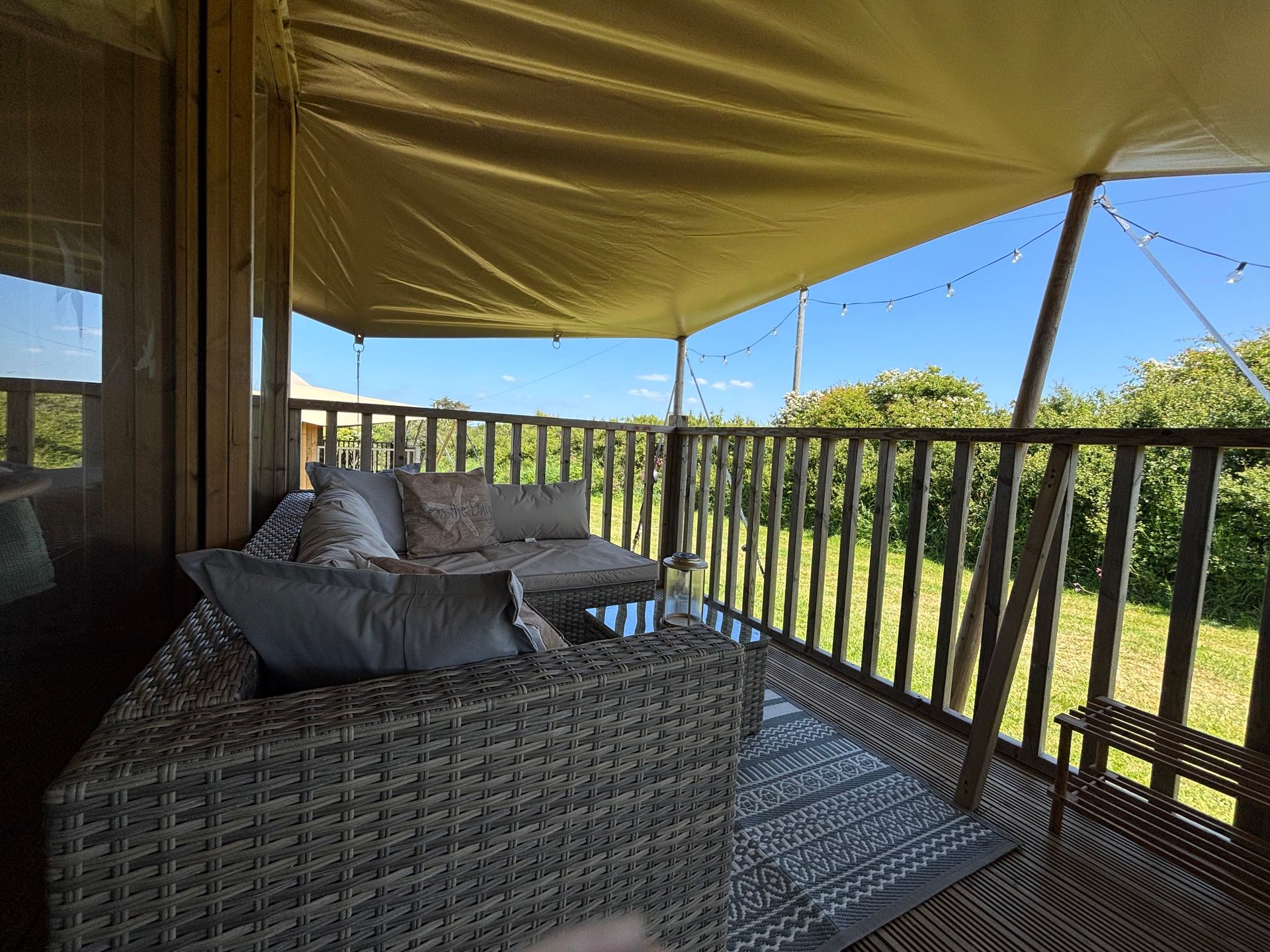 Covered outdoor patio with wicker furniture, overlooking a green landscape under a blue sky.