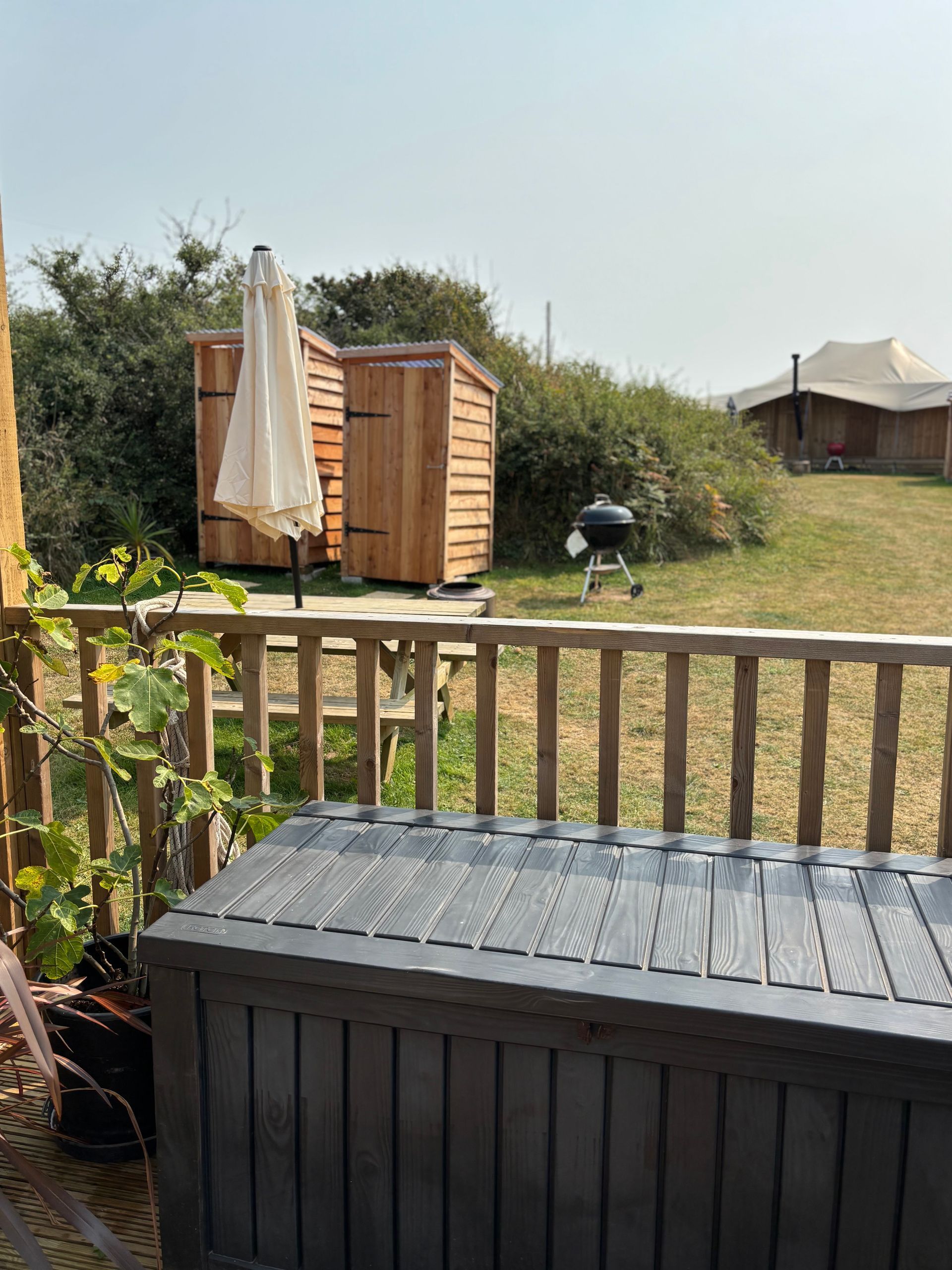 Wooden deck with outdoor storage, picnic table, grill, and two wooden outhouses. A tent in the distance.