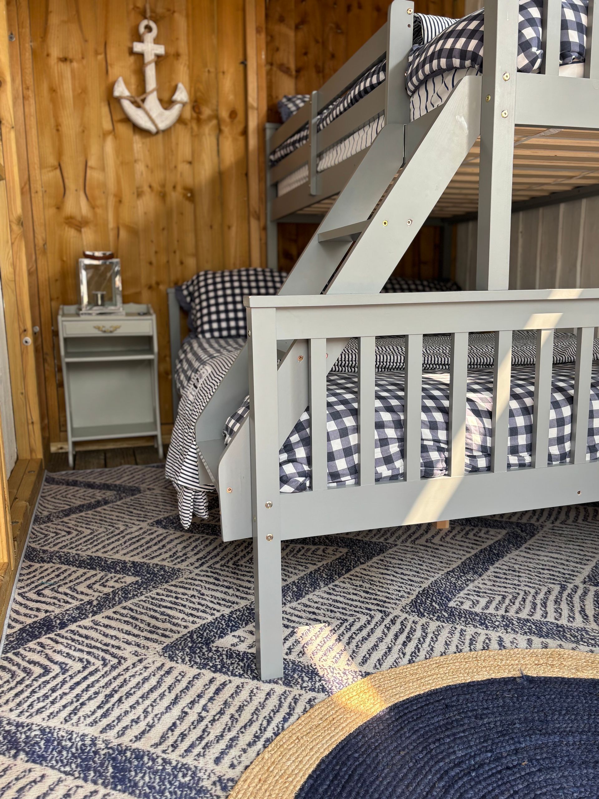 Bedroom with wooden walls, grey bunk beds, blue and white patterned bedding, and a patterned rug.