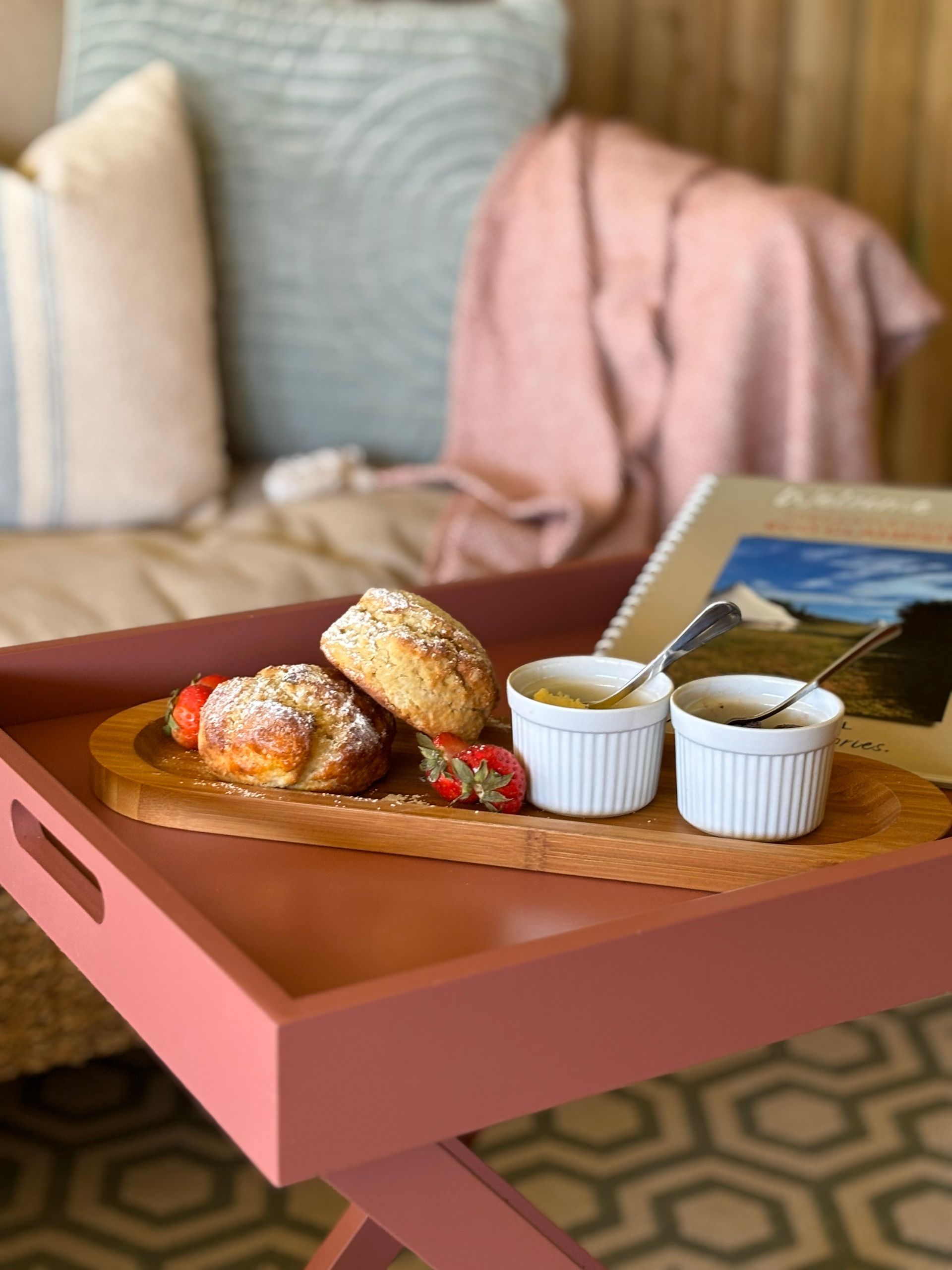 Breakfast tray with pastries, strawberries, and ramekins on a pink table, set in a cozy interior.