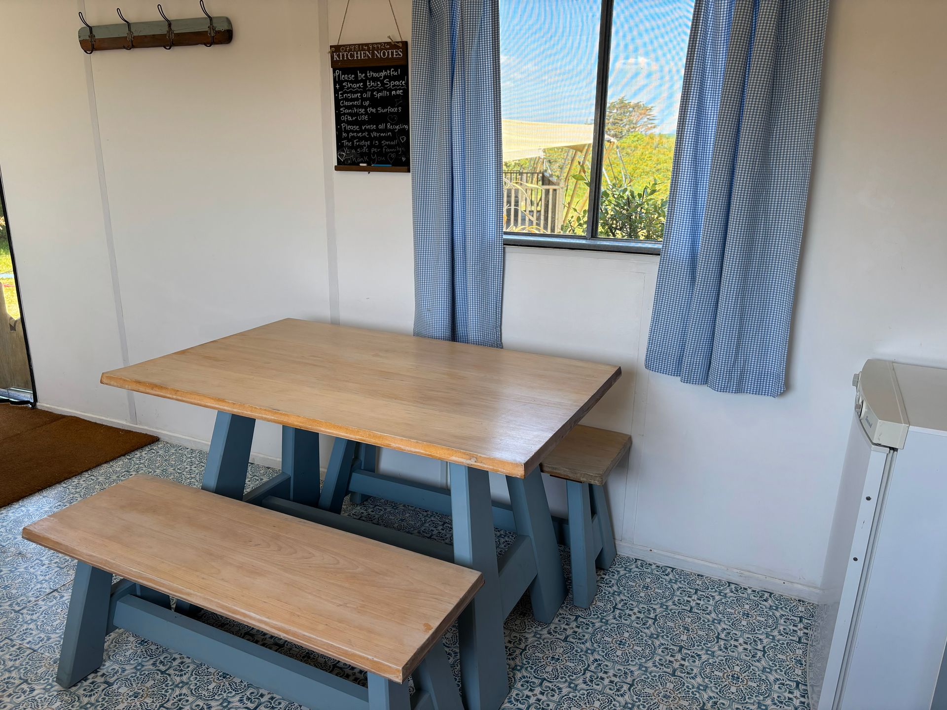 Indoor dining area with light wood table and bench, blue painted legs, window with blue striped curtains.