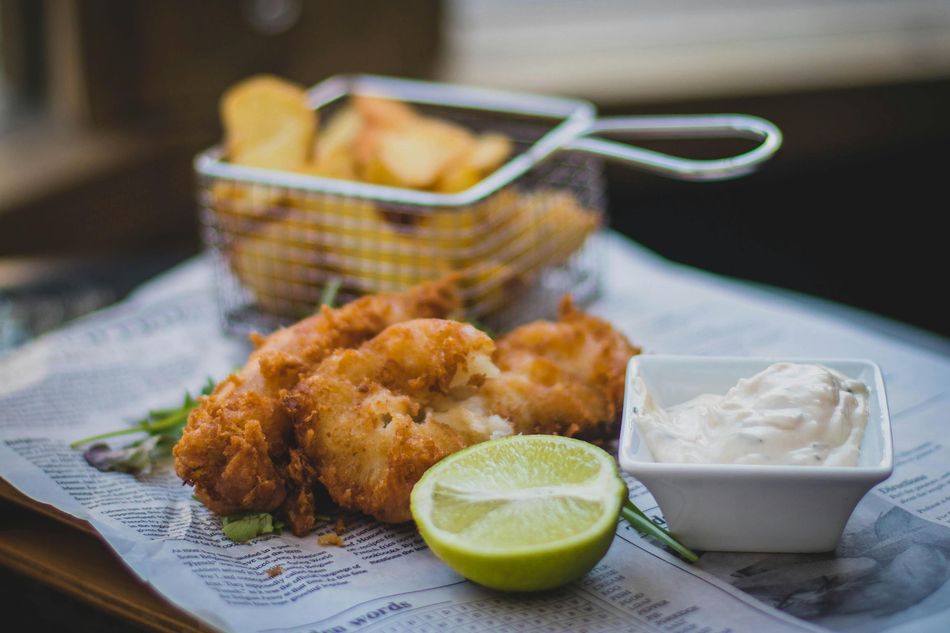 Fish and chips with lime and sauce, served on newspaper, with fries in a wire basket.