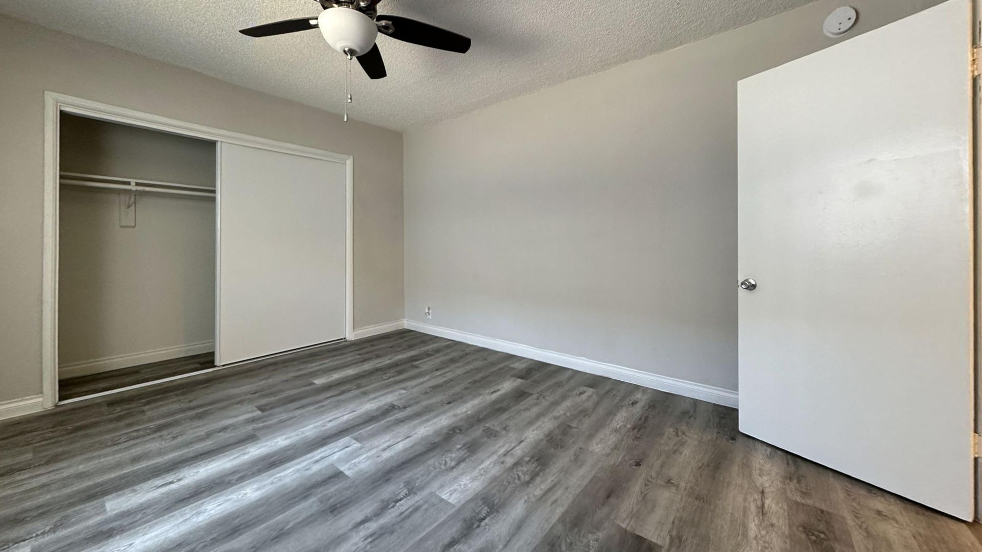 Empty bedroom with gray laminate flooring, white doors, and a ceiling fan.