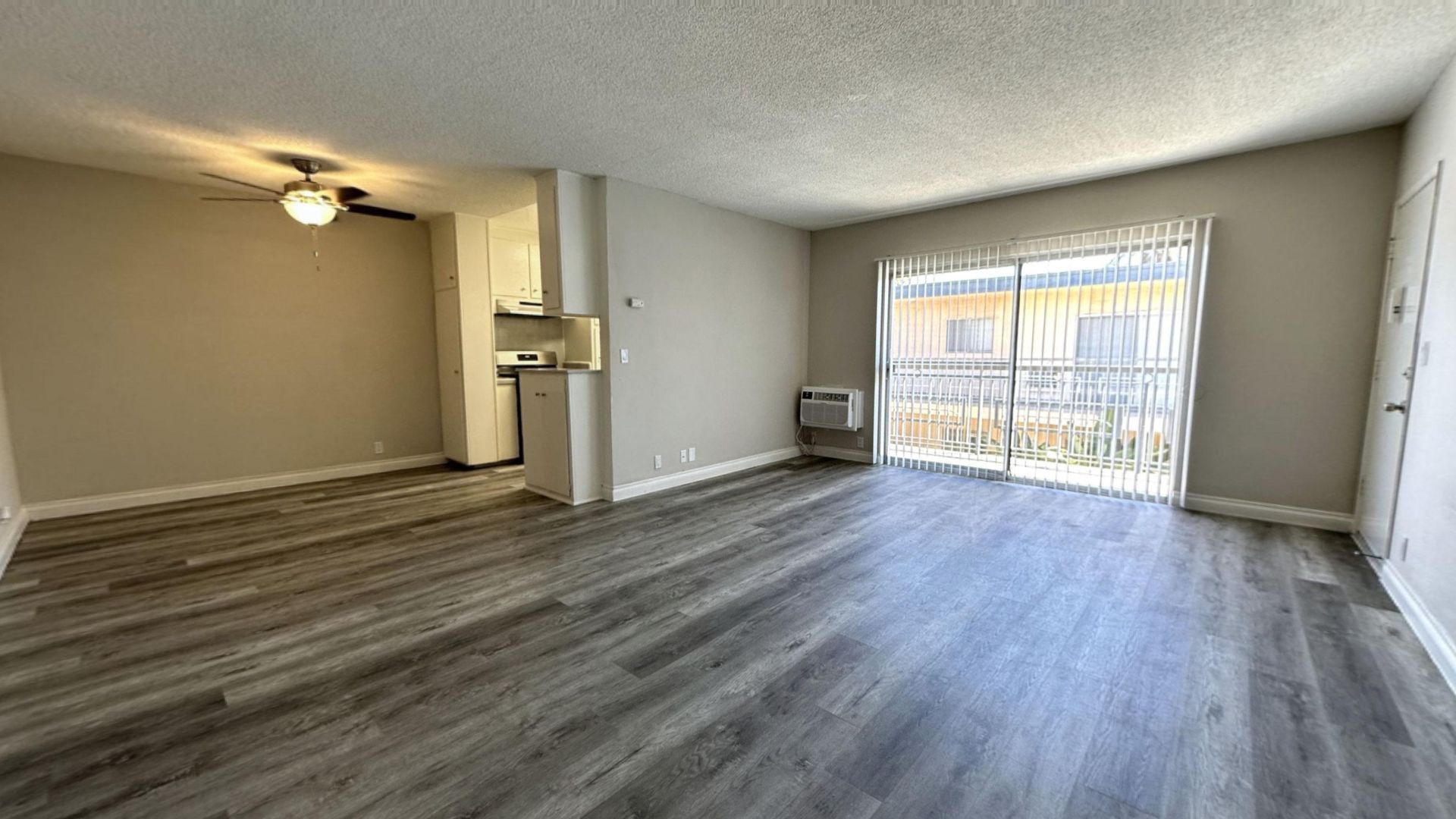 Empty living space with gray wood-look flooring, a sliding glass door, and a small kitchen.