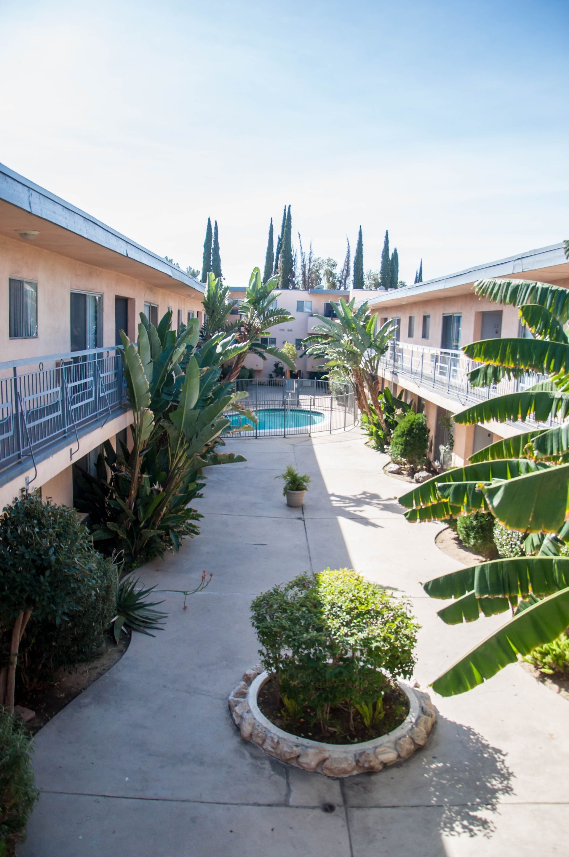 Courtyard of apartment buildings with a pool, palm trees, and clear sky.