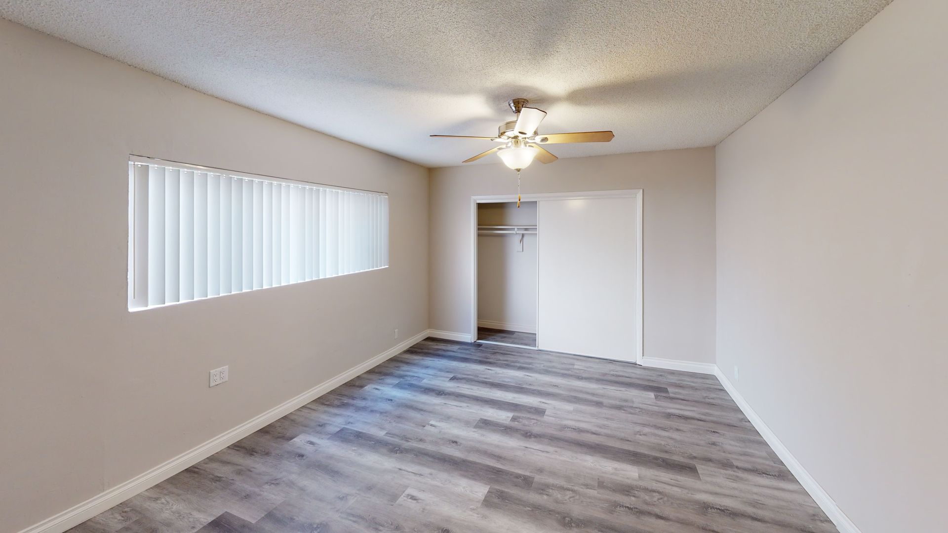Empty bedroom with wood-look flooring, a window with blinds, a closet, and a ceiling fan.