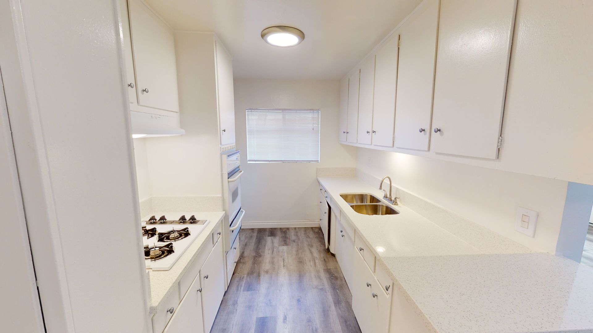 Narrow, white kitchen with countertops, cabinets, and a window.