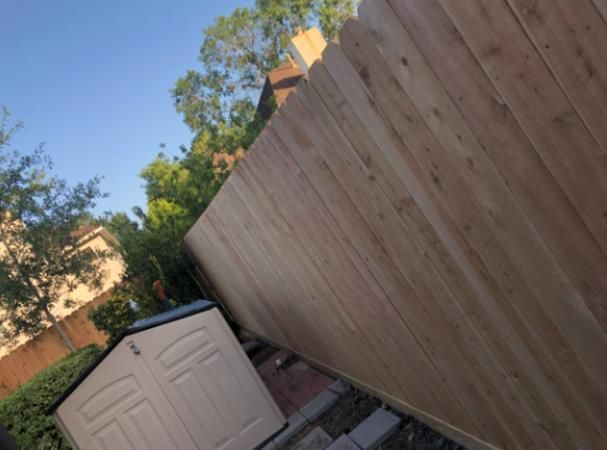 Stack of vertical slat replacement fence panels in a residential backyard, prepared for installation.