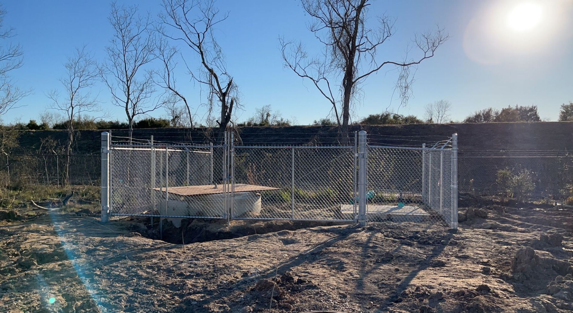 Construction site with a tan and black fence being built alongside a light-colored building.