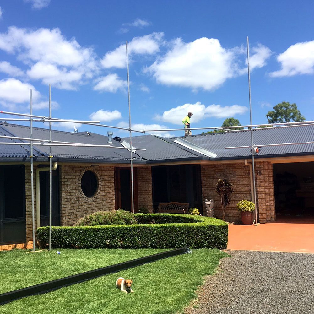 A Man is Standing on the Roof of a House — Monty's Metal Roofing In Ocean Shores, NSW