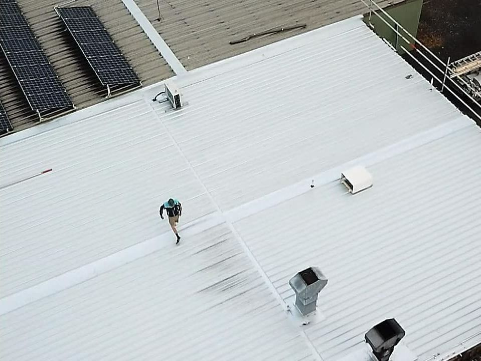 An Aerial View of a Man Standing on Top of a White Roof — Monty's Metal Roofing In Ocean Shores, NSW