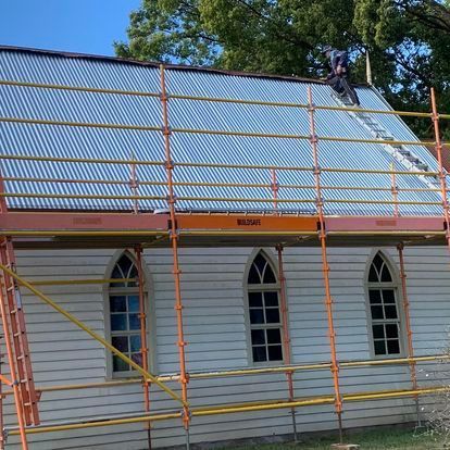 A Man is Standing on the Roof of a Building With Scaffolding Around It — Monty's Metal Roofing In Ocean Shores, NSW