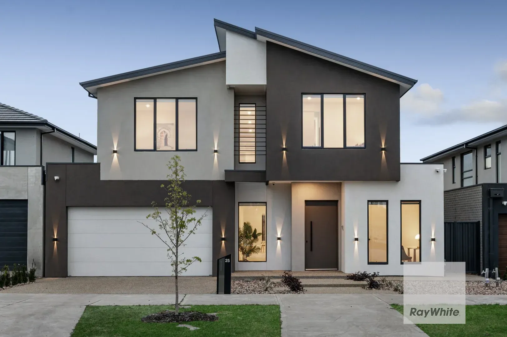 Modern two-story gray house with a double garage and small front lawn at dusk