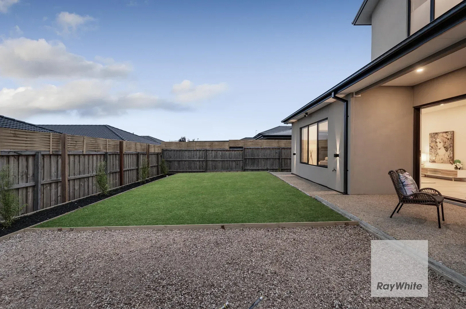 Backyard patio with gravel, green lawn, wooden fence, and covered outdoor seating beside a house