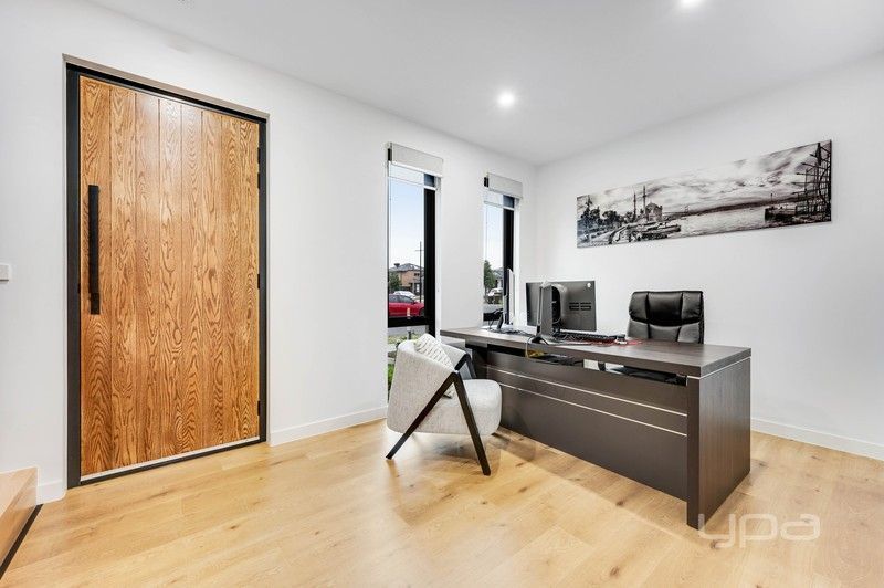 Modern home office with wooden desk, black chair, and a large wood front door on light wood floors