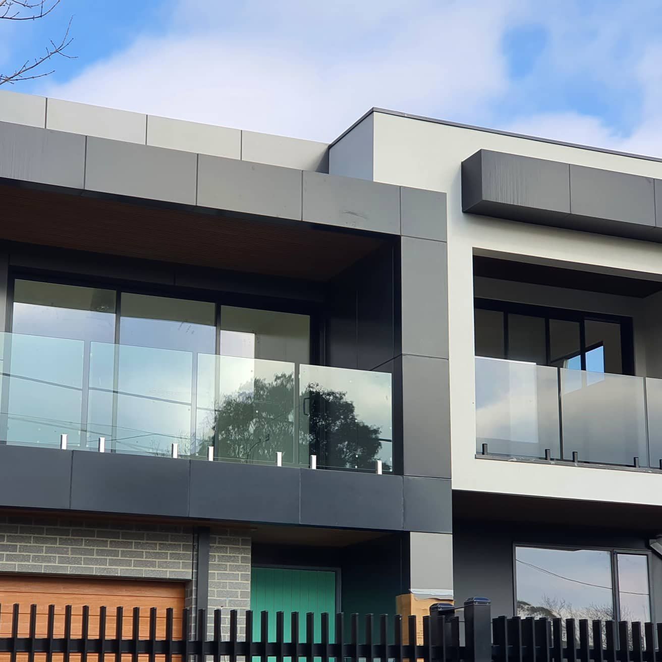 Modern two-story house with large glass balconies, gray facade, and wooden accents under a blue sky