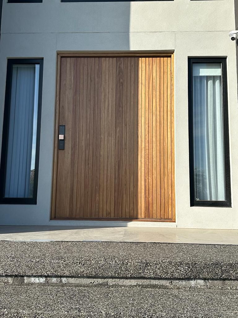 Modern house entrance with a large wooden front door and tall narrow windows on either side.