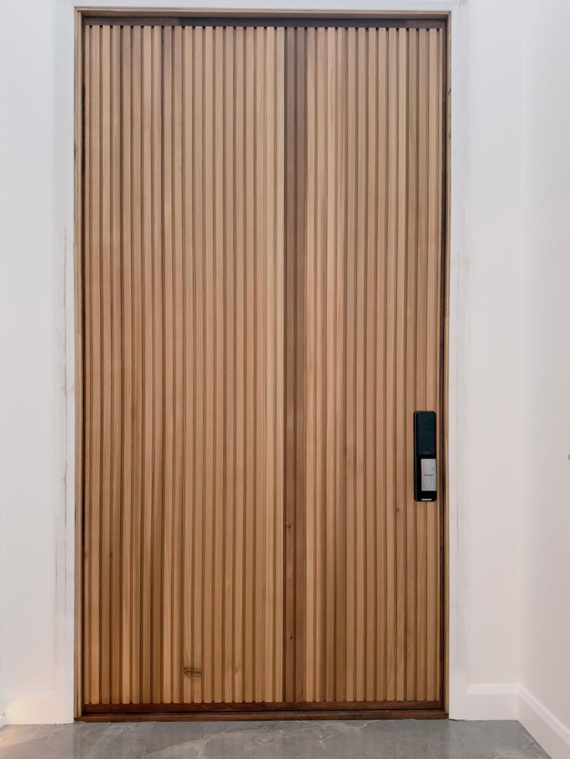 Wood-paneled front door with a black handle set in a white hallway wall.